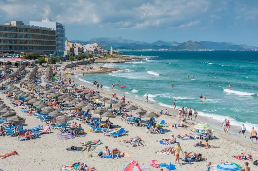 Una playa concurrida con bañistas, sombrillas y agua turquesa.