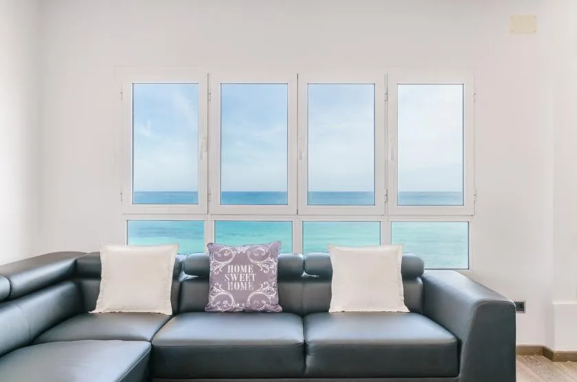 Una sala de estar con asientos oscuros junto a grandes ventanas con vista al mar.