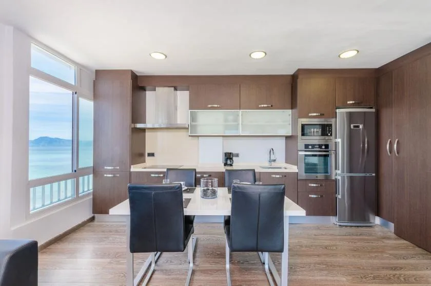 Cocina y comedor modernos con gabinetes oscuros y una ventana amplia con vista al agua.