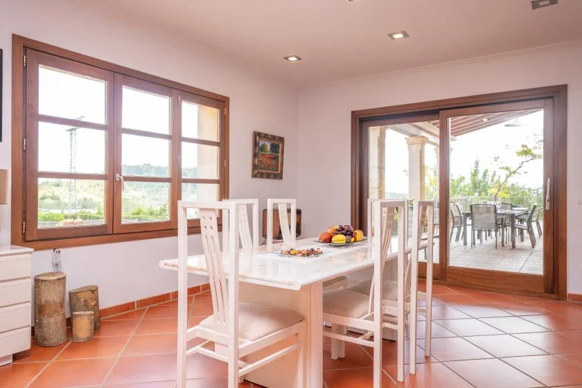 A dining area with a white table and seating beside large windows.