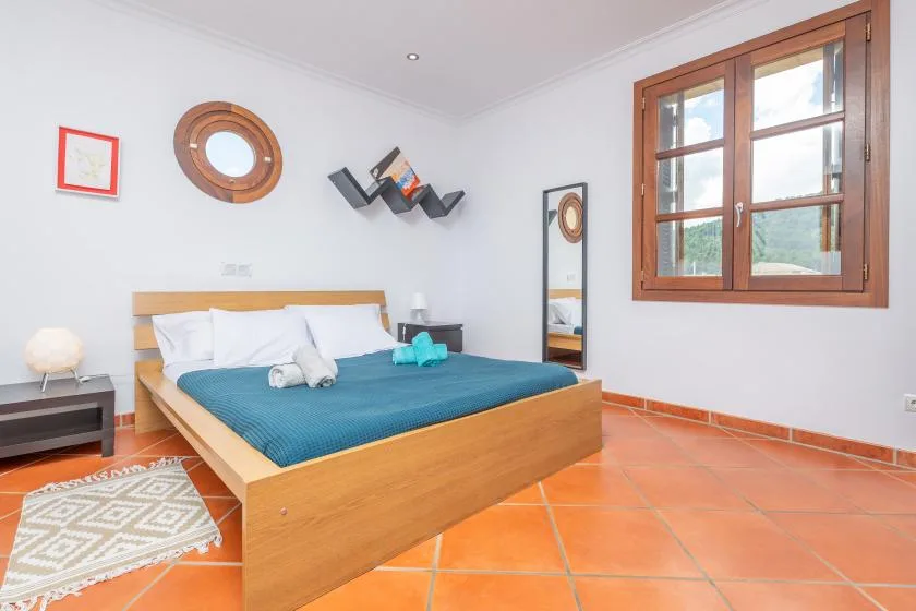 A bedroom with a wooden bed, blue bedding, and a window.