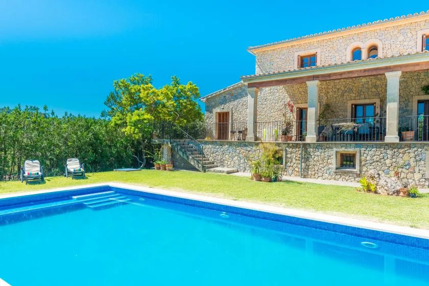 A swimming pool in front of a stone house and green lawn.