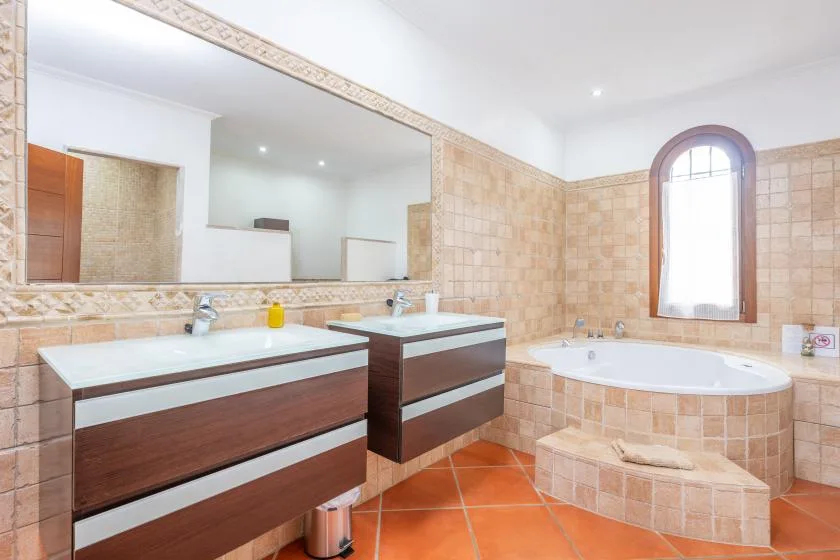 A tiled bathroom features two vanities and a bathtub beneath an arched window.