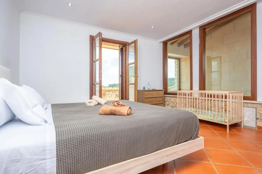 A bedroom with a large bed and a wooden crib beside the windows.