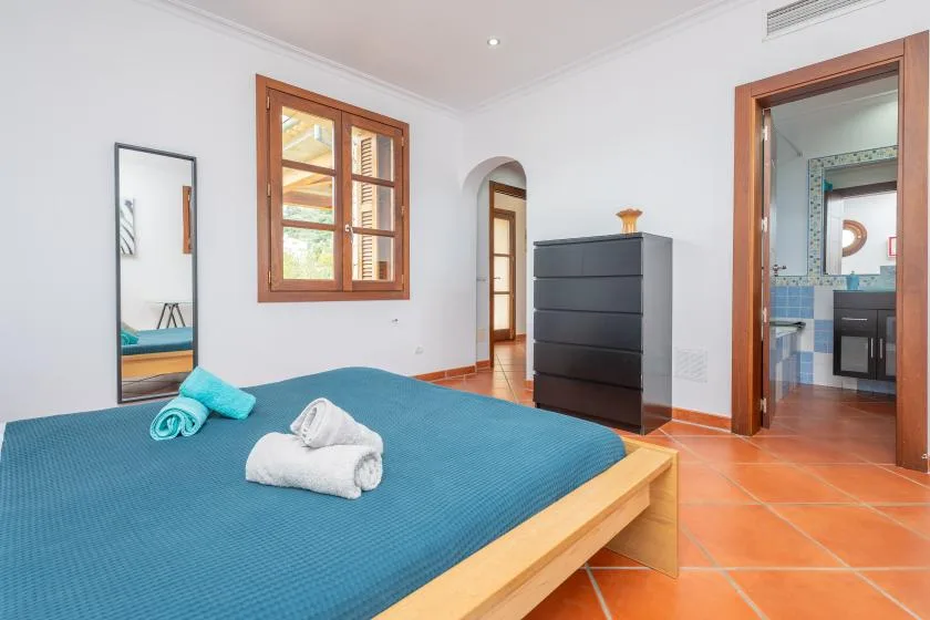 A bedroom with a bed, a wooden-framed window, and a dark dresser.