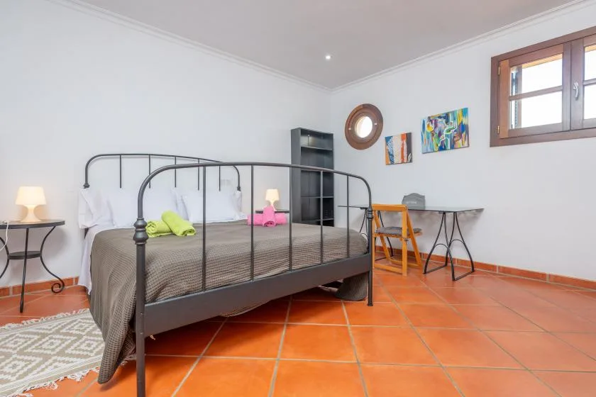 A bedroom with a metal-framed bed, colorful wall art, and a high window.