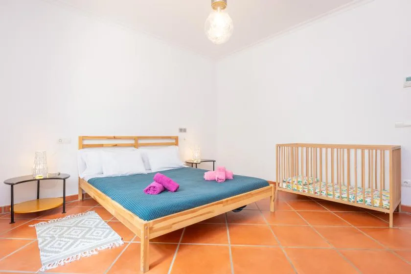 A bright bedroom with a wooden bed and a crib beside it.