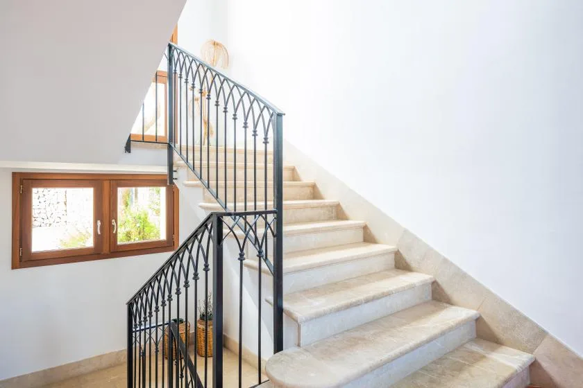 A bright interior staircase with pale steps and dark metal railings.