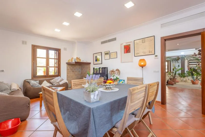 A bright dining and living area features a table set with flowers beside framed wall art.