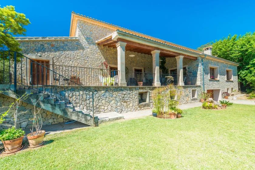 A stone house with a covered porch overlooks a grassy yard.