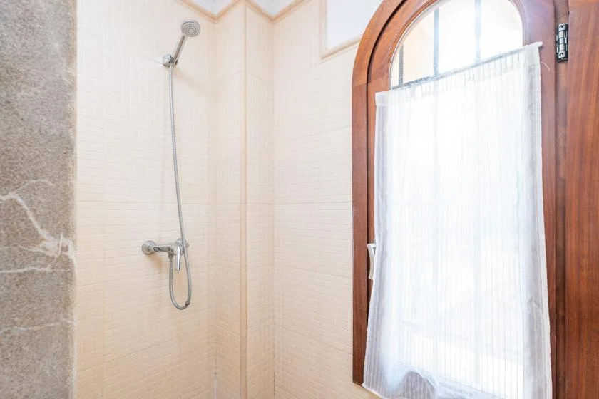 A tiled bathroom with a wall-mounted shower beside an arched window.