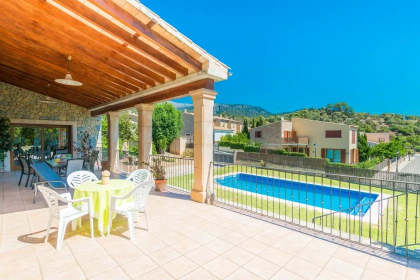A covered patio with outdoor seating overlooks a fenced swimming pool.