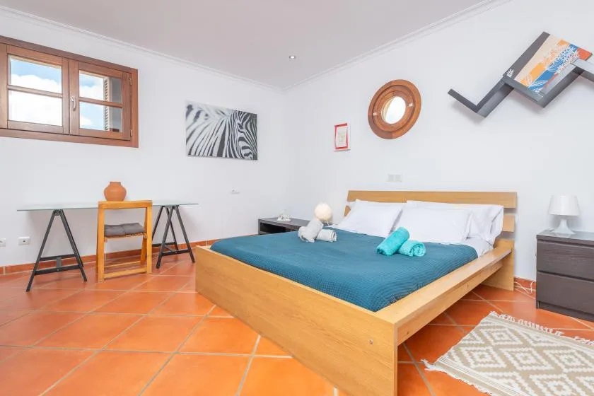 A bedroom with a wooden bed, teal bedding, and orange floor tiles.