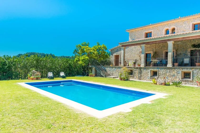 A swimming pool sits on a grassy lawn beside a stone house.