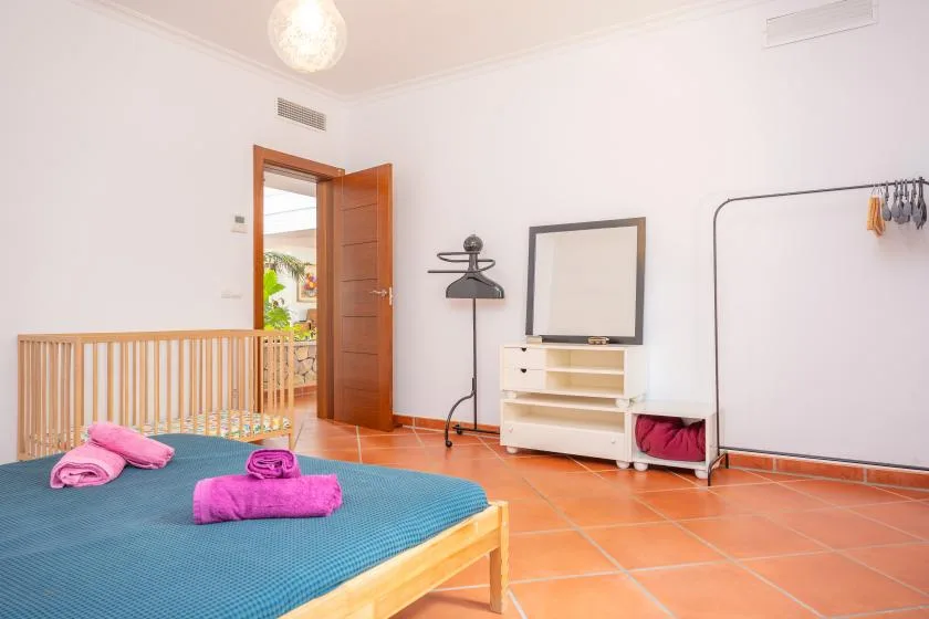 A bright bedroom with a low bed, colorful towels, and a small dresser.