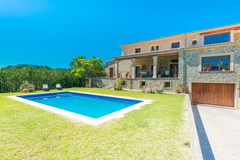 A stone house overlooks a rectangular swimming pool and lawn.
