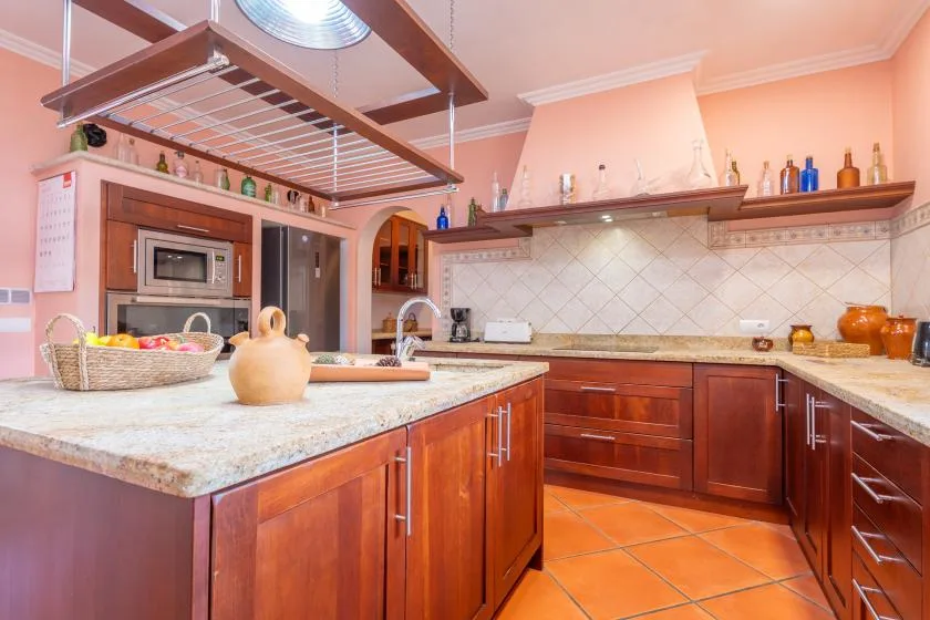 A kitchen with wooden cabinets, tiled walls, and a large central counter.