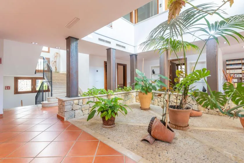 A bright atrium with potted plants, stone planters, and a tiled walkway.