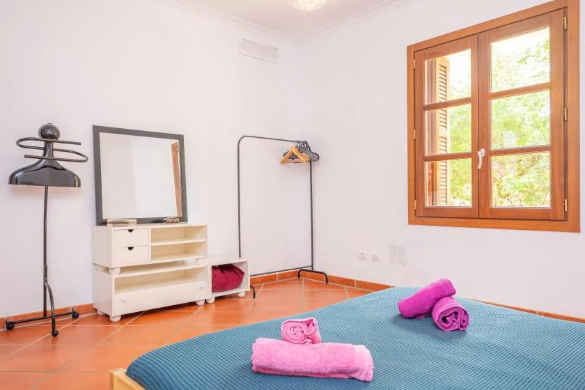 A bedroom with a blue bedspread, pink towels, and a wooden-framed window.