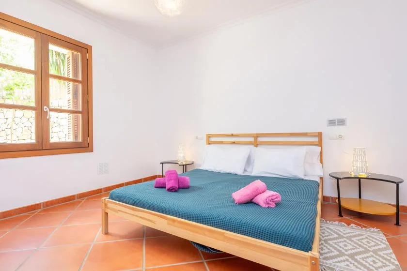 A bedroom with a wooden bed, blue bedding, and a window overlooking greenery.