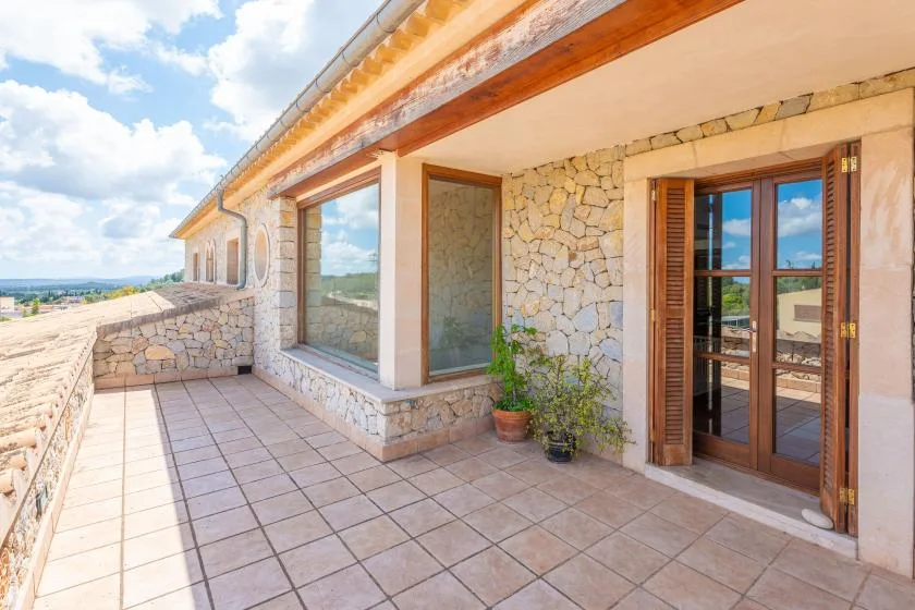 A tiled terrace runs along a stone exterior wall with large windows and a glazed door.