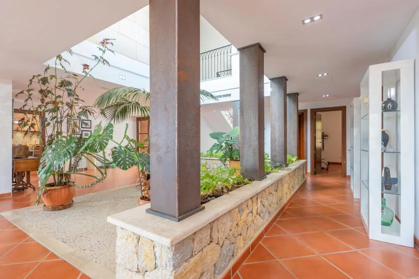 A tiled hallway opens onto a bright indoor atrium with plants and stonework.