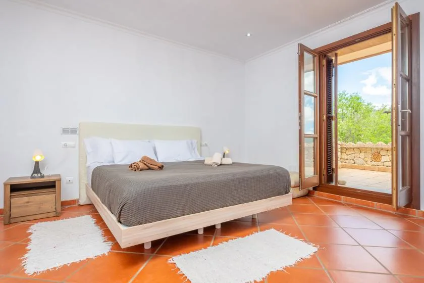 A bedroom with a neatly made bed and open doors to a patio.