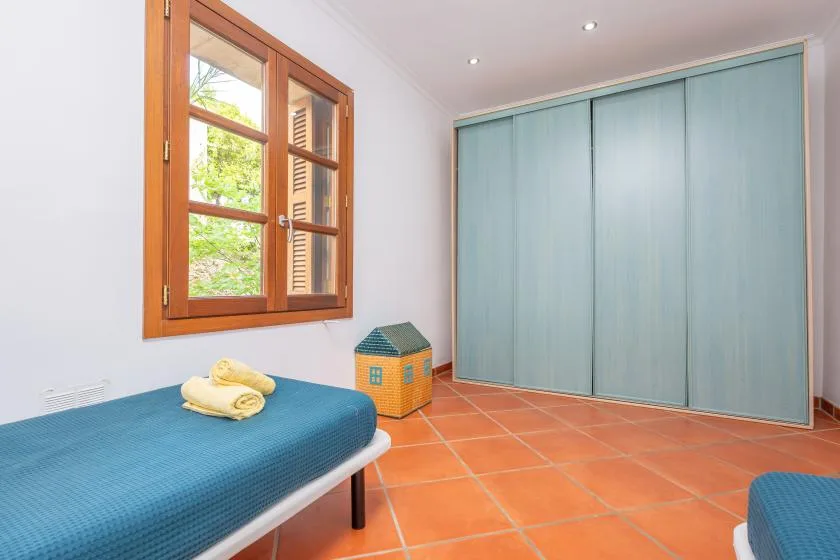 A bright room with a blue-covered bed, a wooden window, and large blue closet doors.