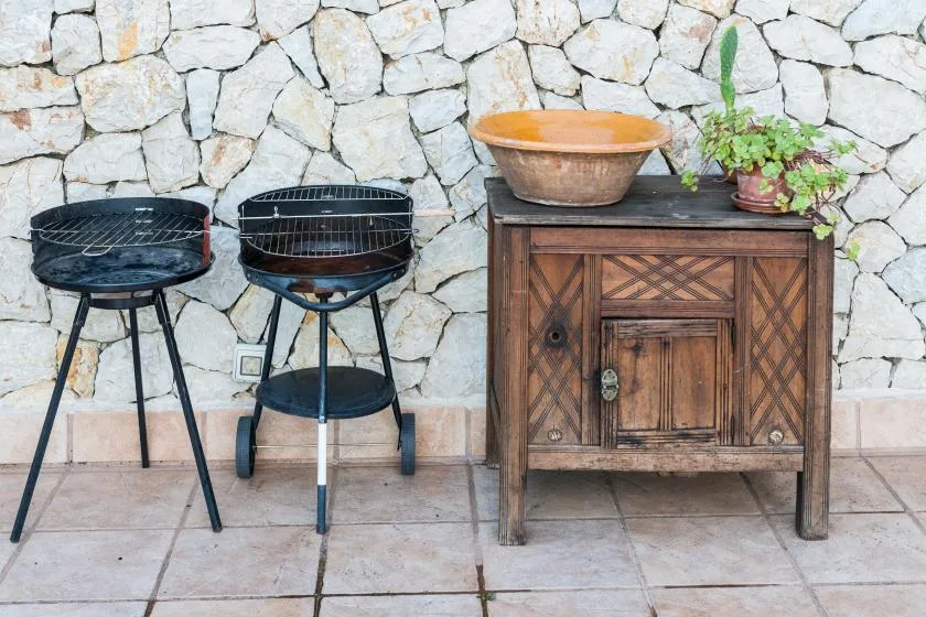 Outdoor patio with two grills beside a wooden cabinet against a stone wall.