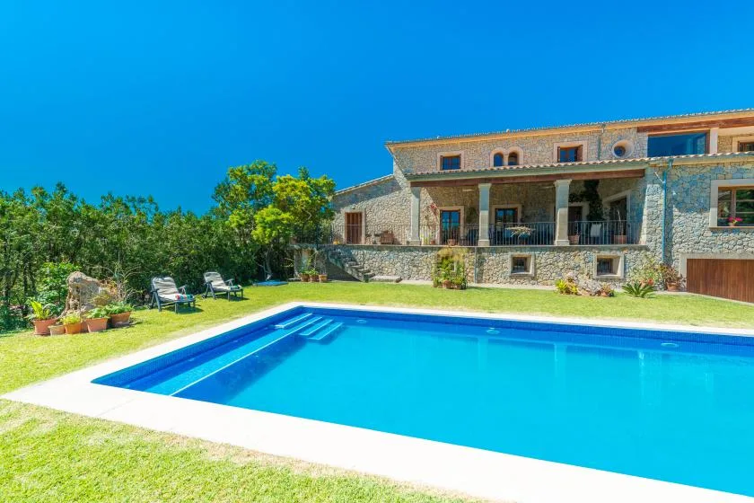 An outdoor swimming pool sits beside a stone house and grassy lawn.