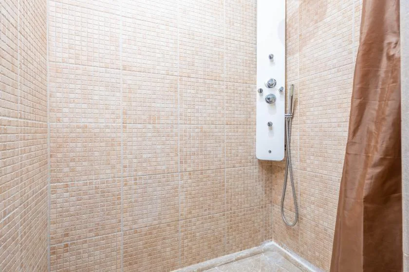 A tiled shower area with a wall-mounted shower panel and a brown curtain.