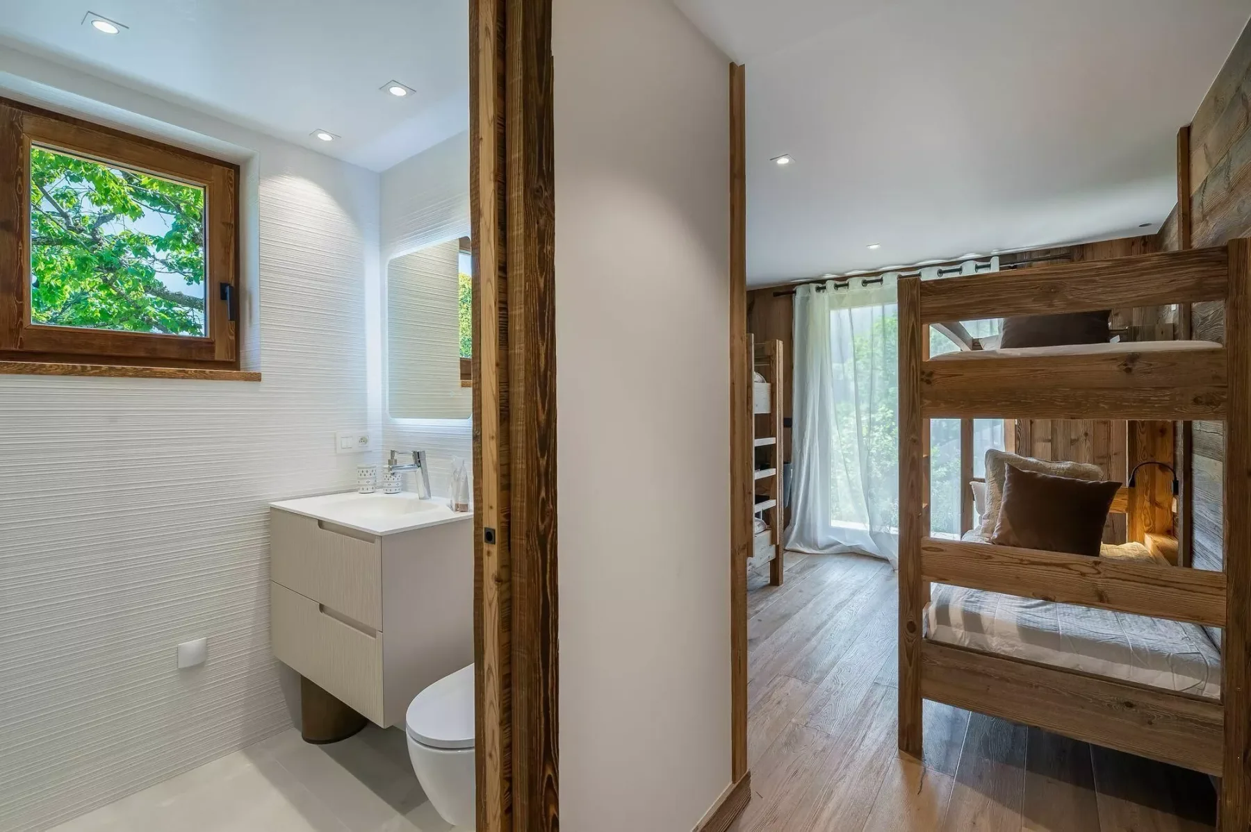 A bedroom with wooden bunk beds sits beside a bright bathroom.