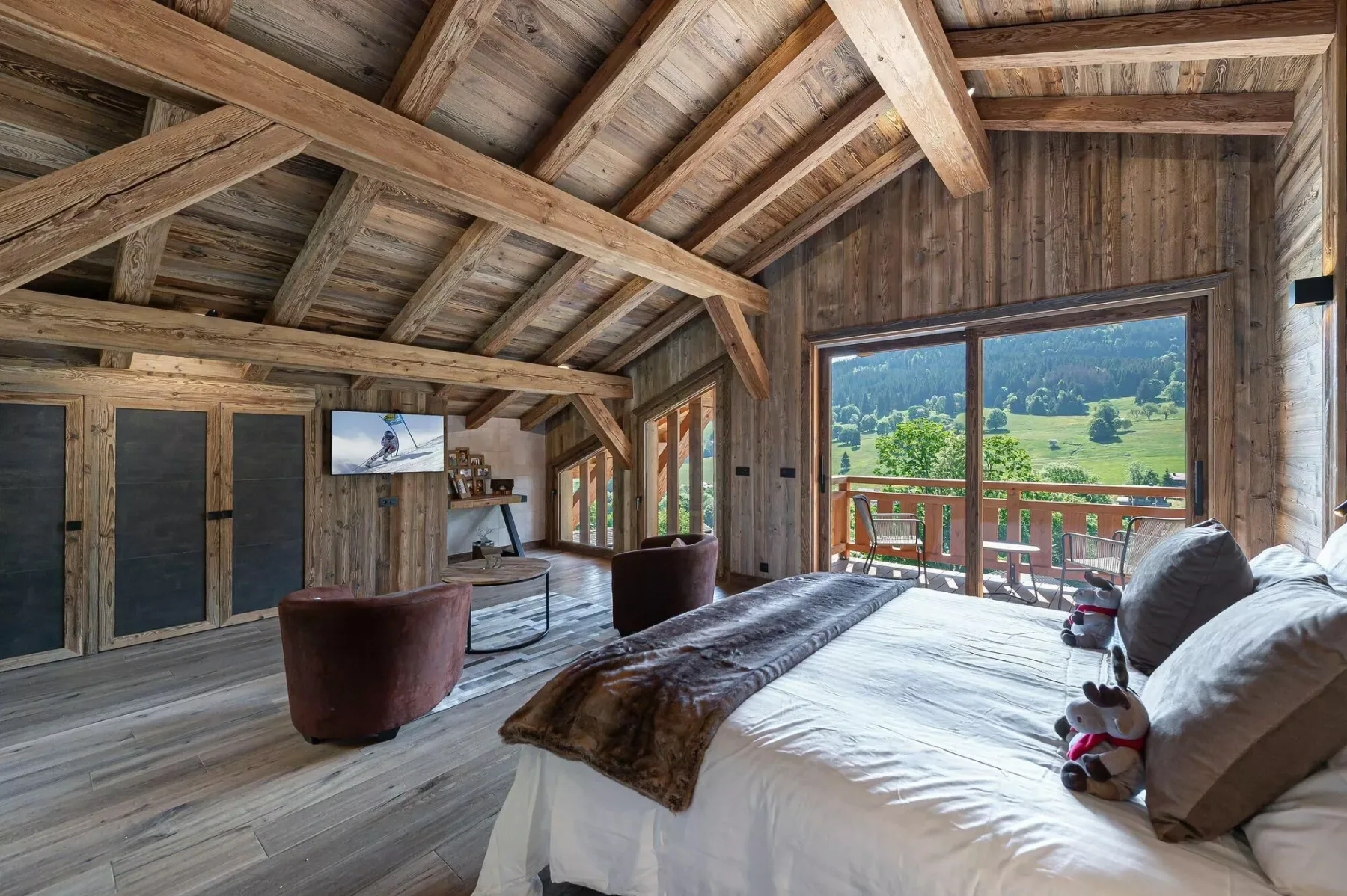 A rustic bedroom with a large bed and sliding glass doors overlooking a green landscape.