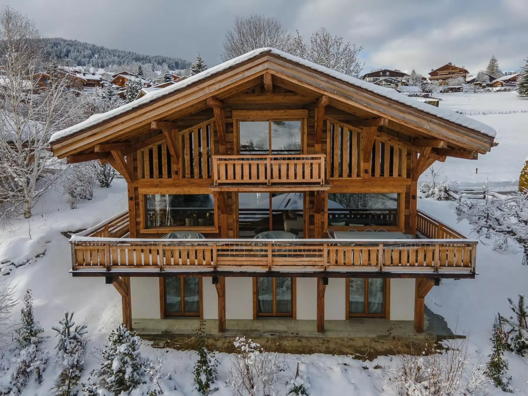 A wooden chalet stands in a snowy landscape, with balconies across its front.