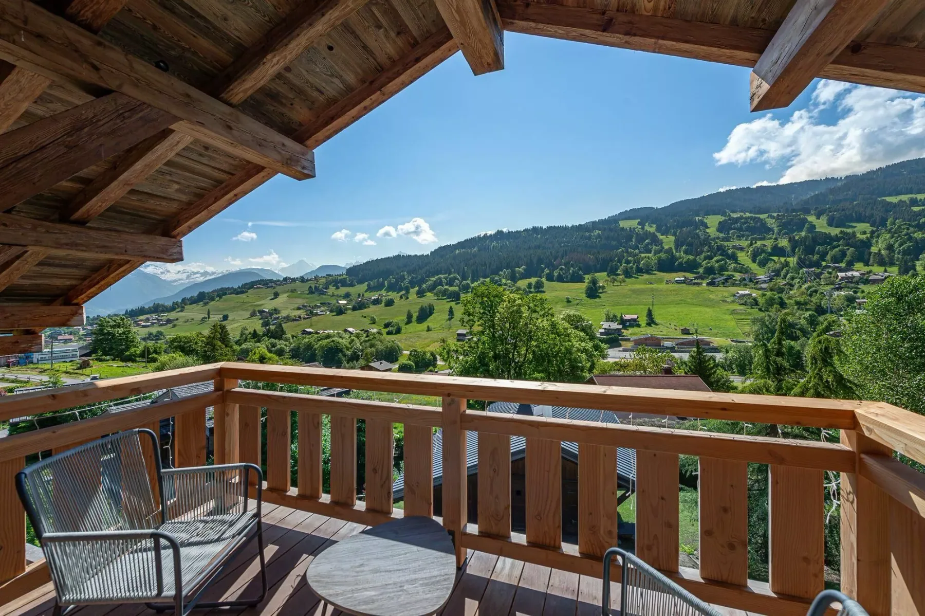 A wooden balcony overlooks a green hillside beneath a clear blue sky.