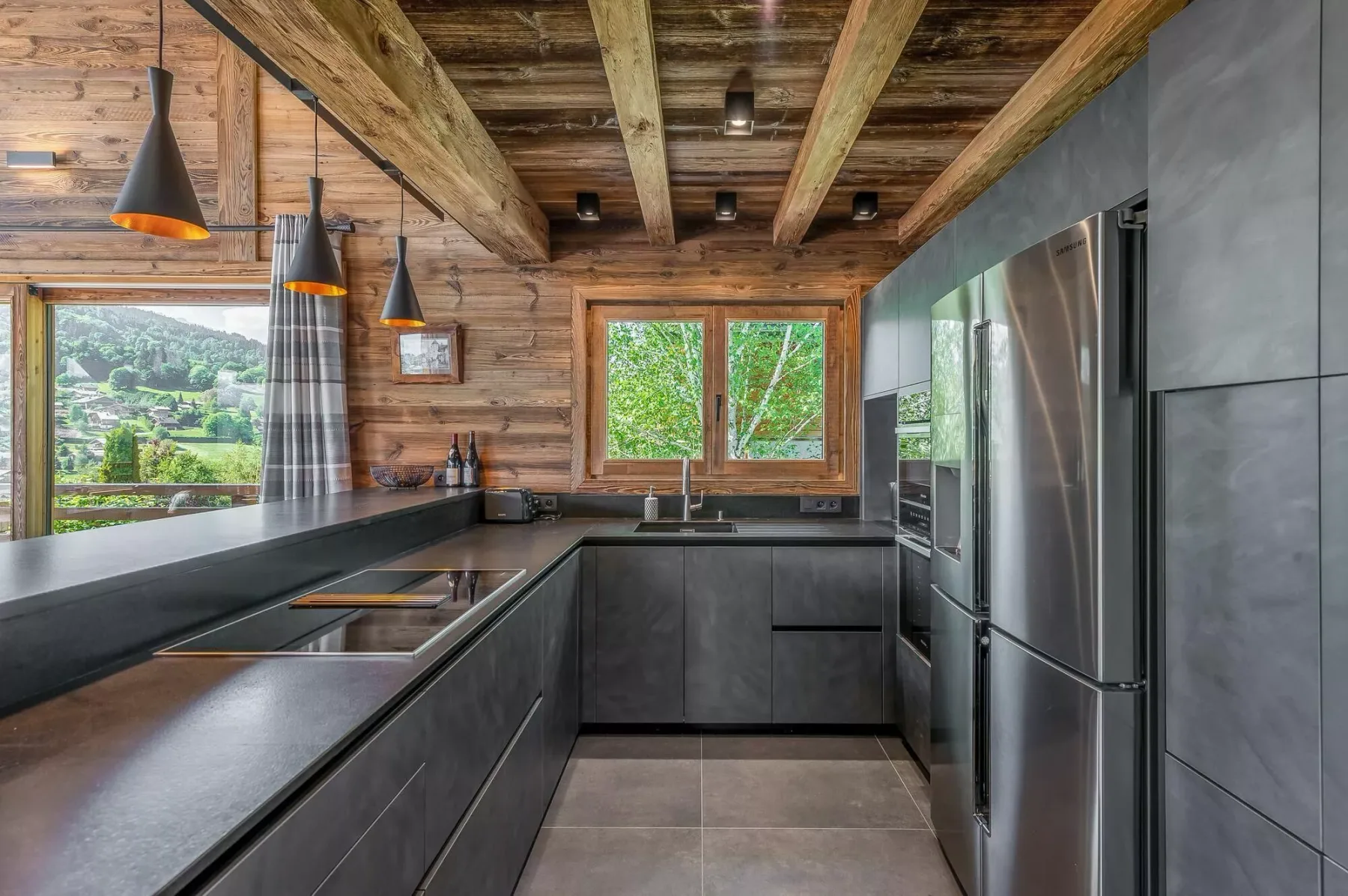 A modern kitchen with dark cabinets, stainless steel appliances, and exposed wooden ceiling beams.