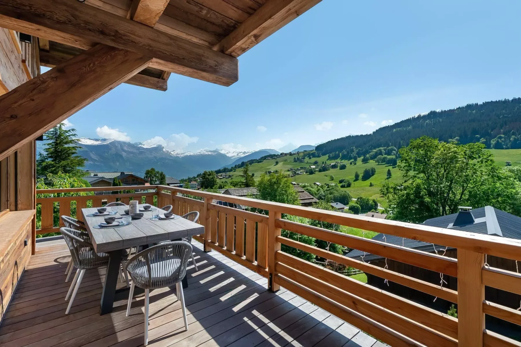 A wooden outdoor deck with a dining table overlooks a green mountain valley.