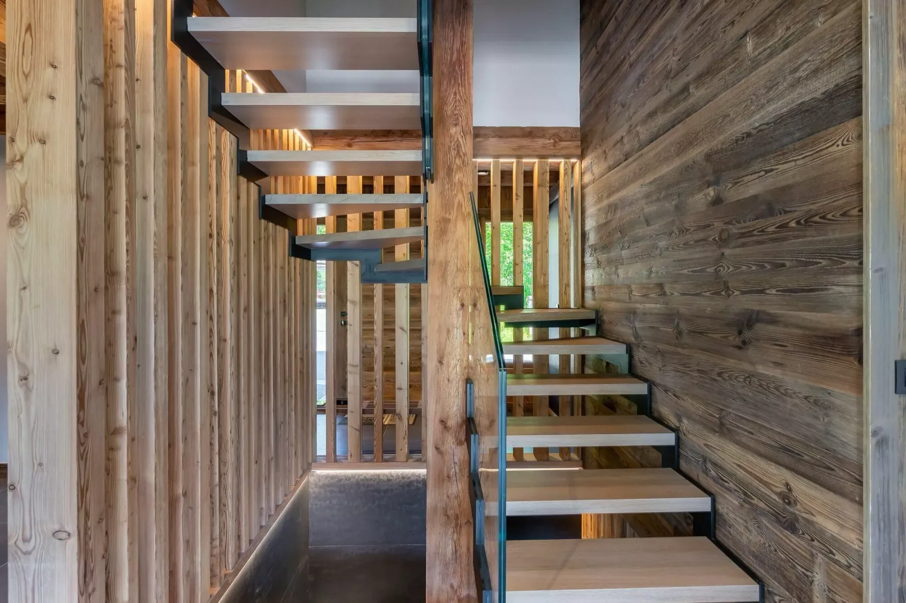 An interior staircase with open wooden steps beside a wood-paneled wall.