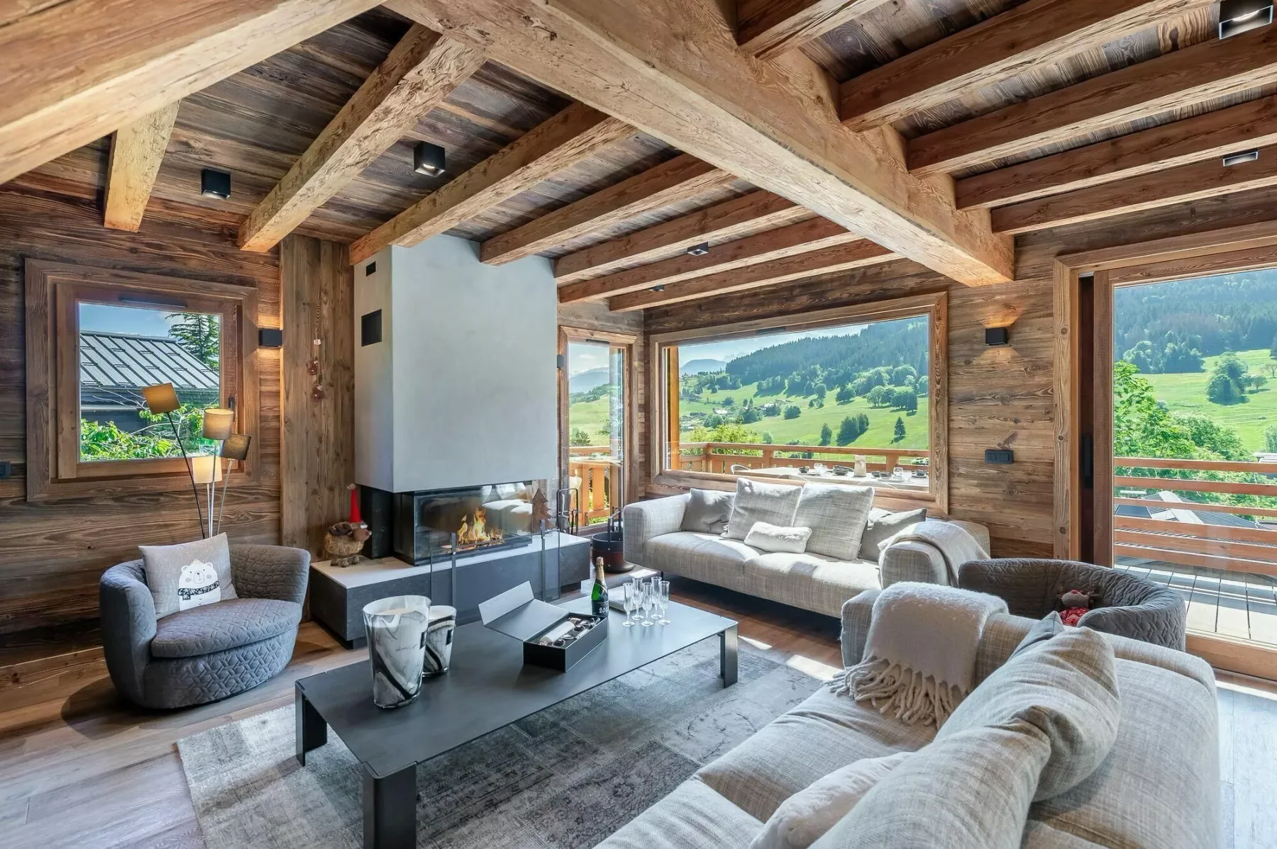 Una sala de estar con vigas de madera, asientos junto a una chimenea y grandes ventanas.