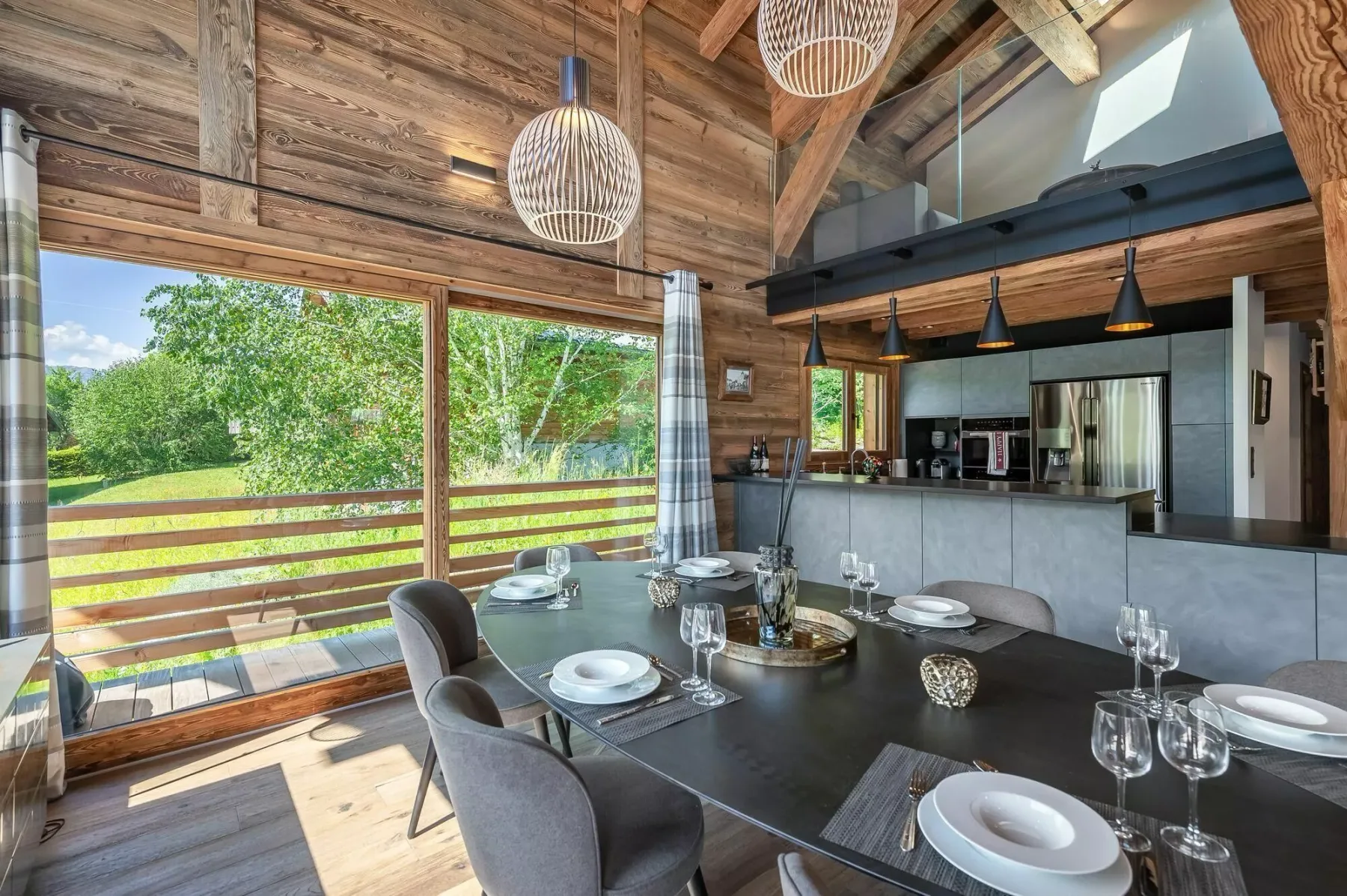 A dining area with a set table beside large windows overlooking greenery.