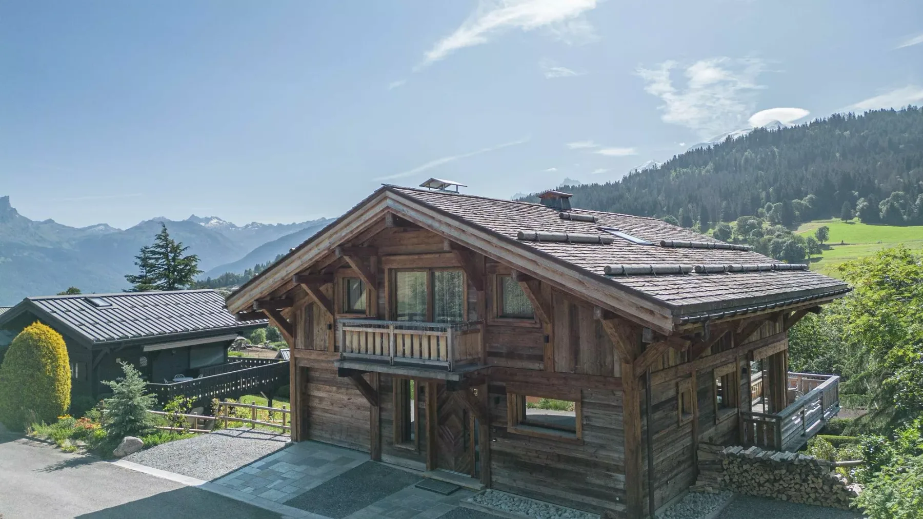 A wooden chalet stands among green hills beneath a partly cloudy sky.