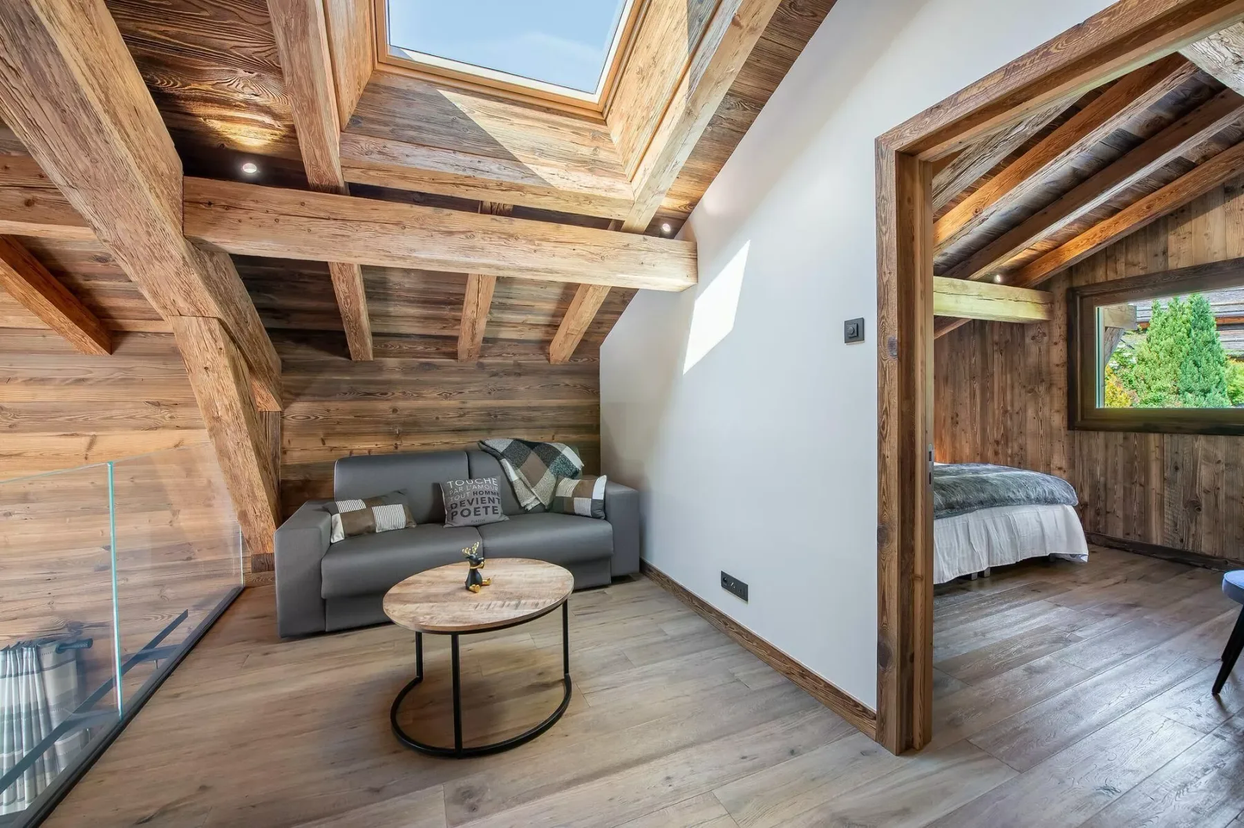 A wood-beamed sitting area with a skylight and an open view into a bedroom.