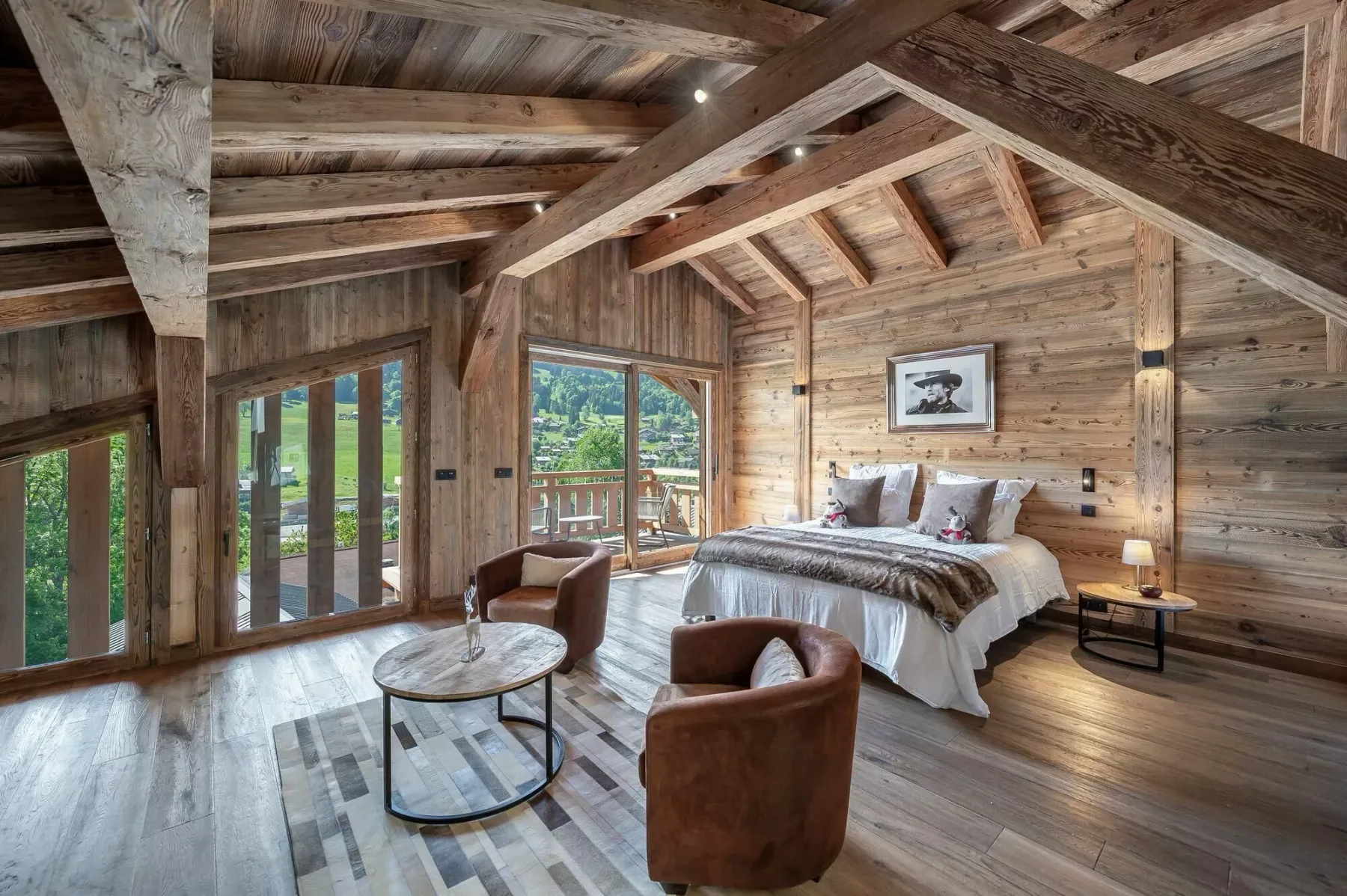 A rustic bedroom with a large bed and seating beneath exposed wooden beams.