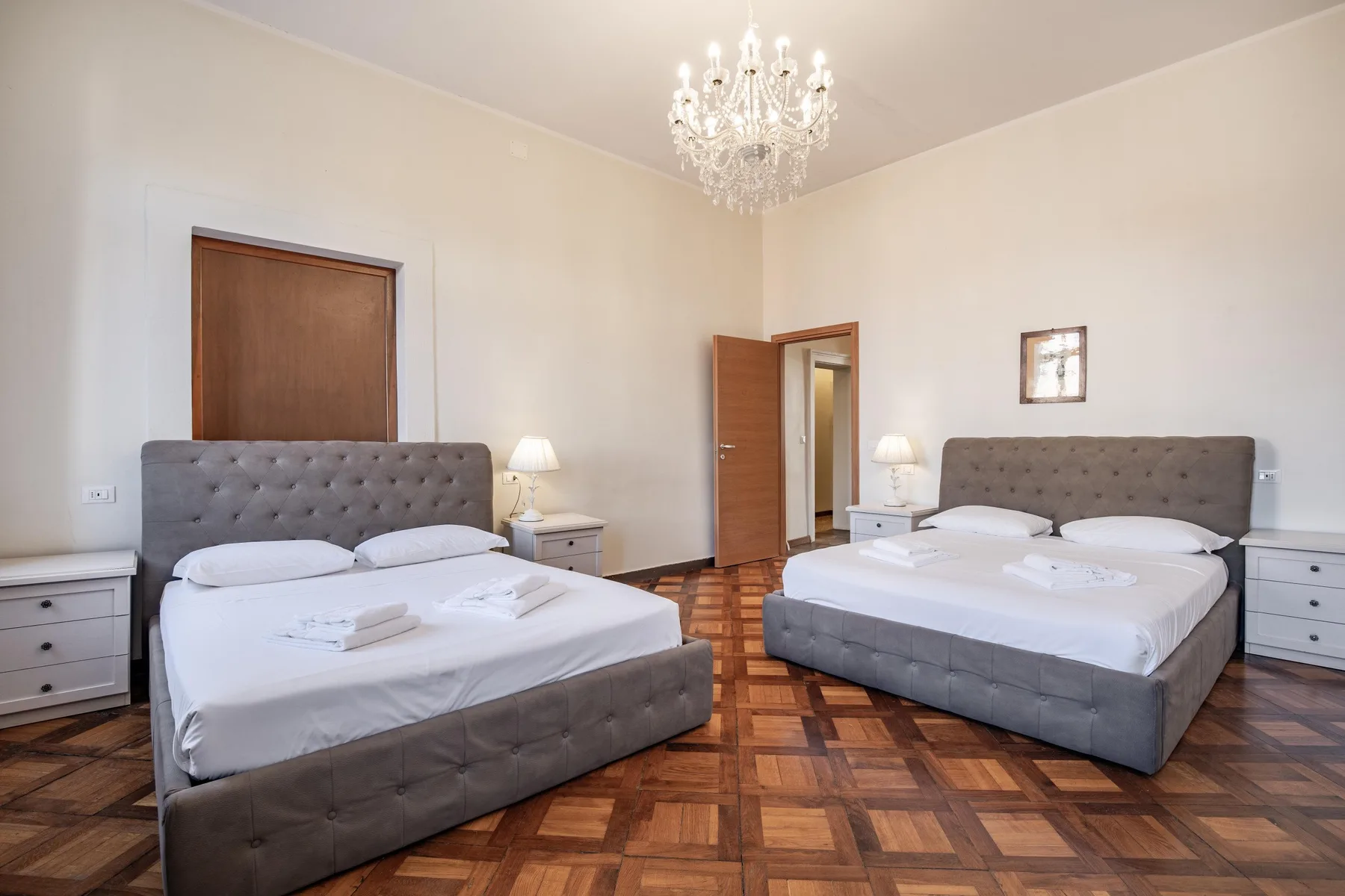 A bedroom with two beds, bedside tables, and a chandelier.