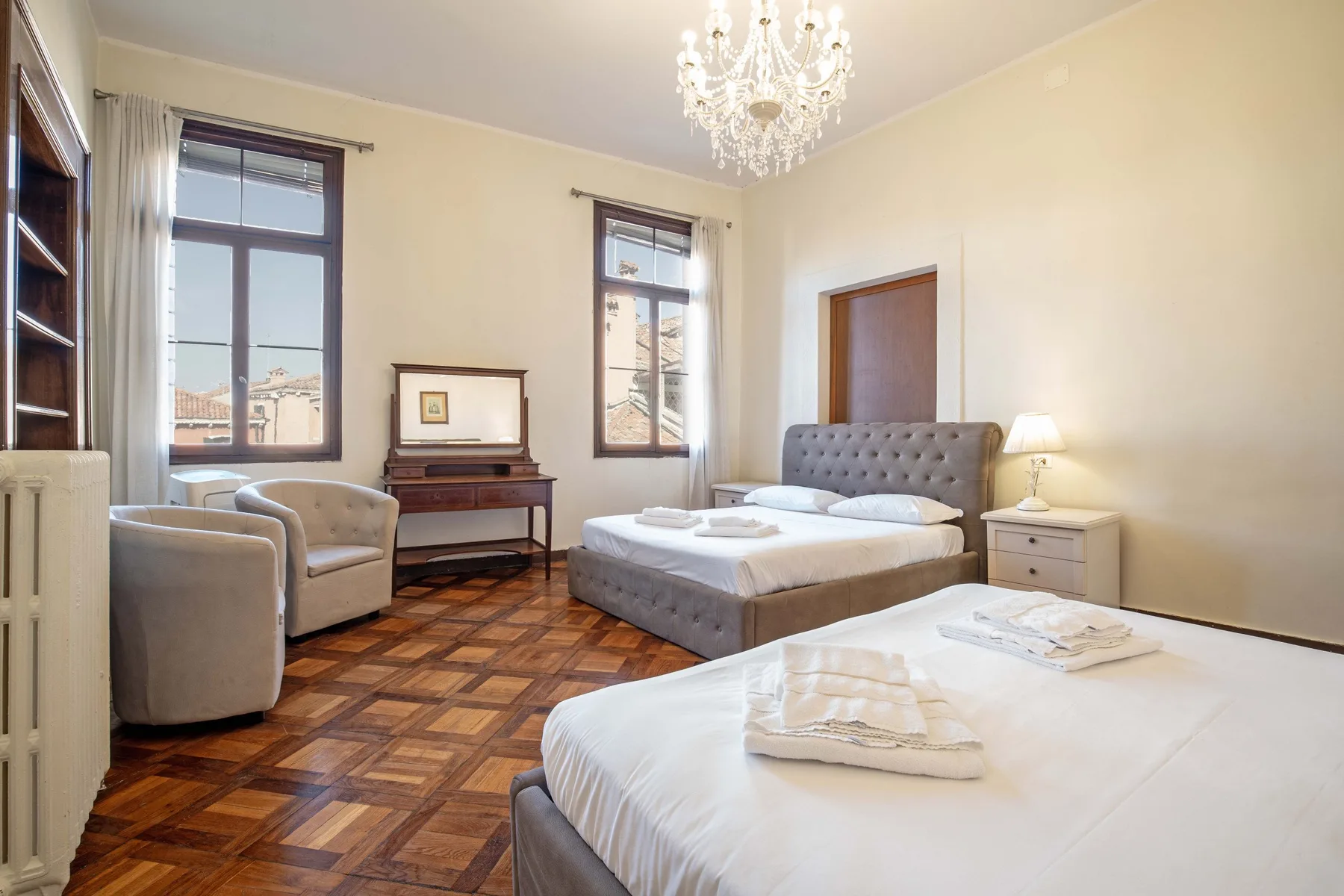 A bedroom with two beds, armchairs, and tall windows.