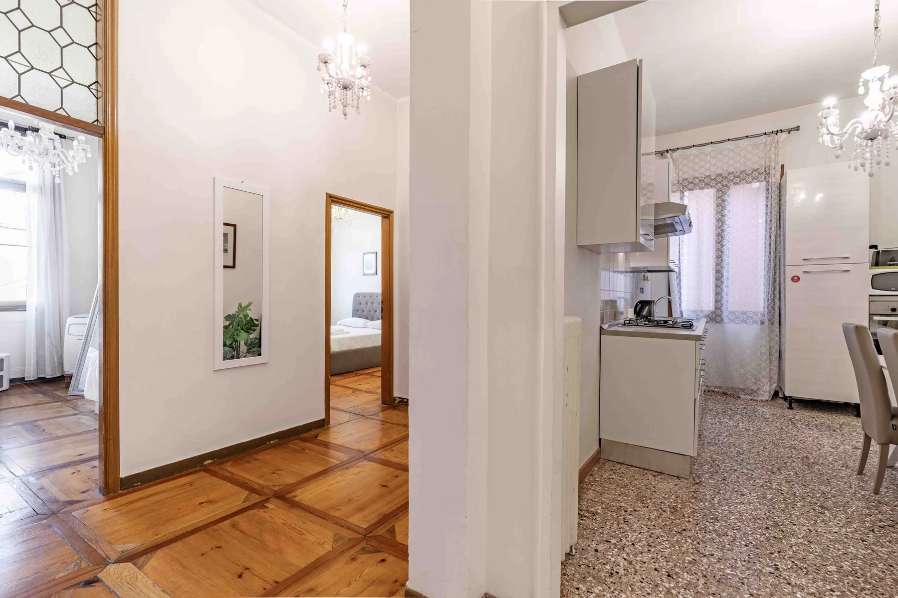 A bright apartment interior shows a wood-floored hallway beside a kitchen.