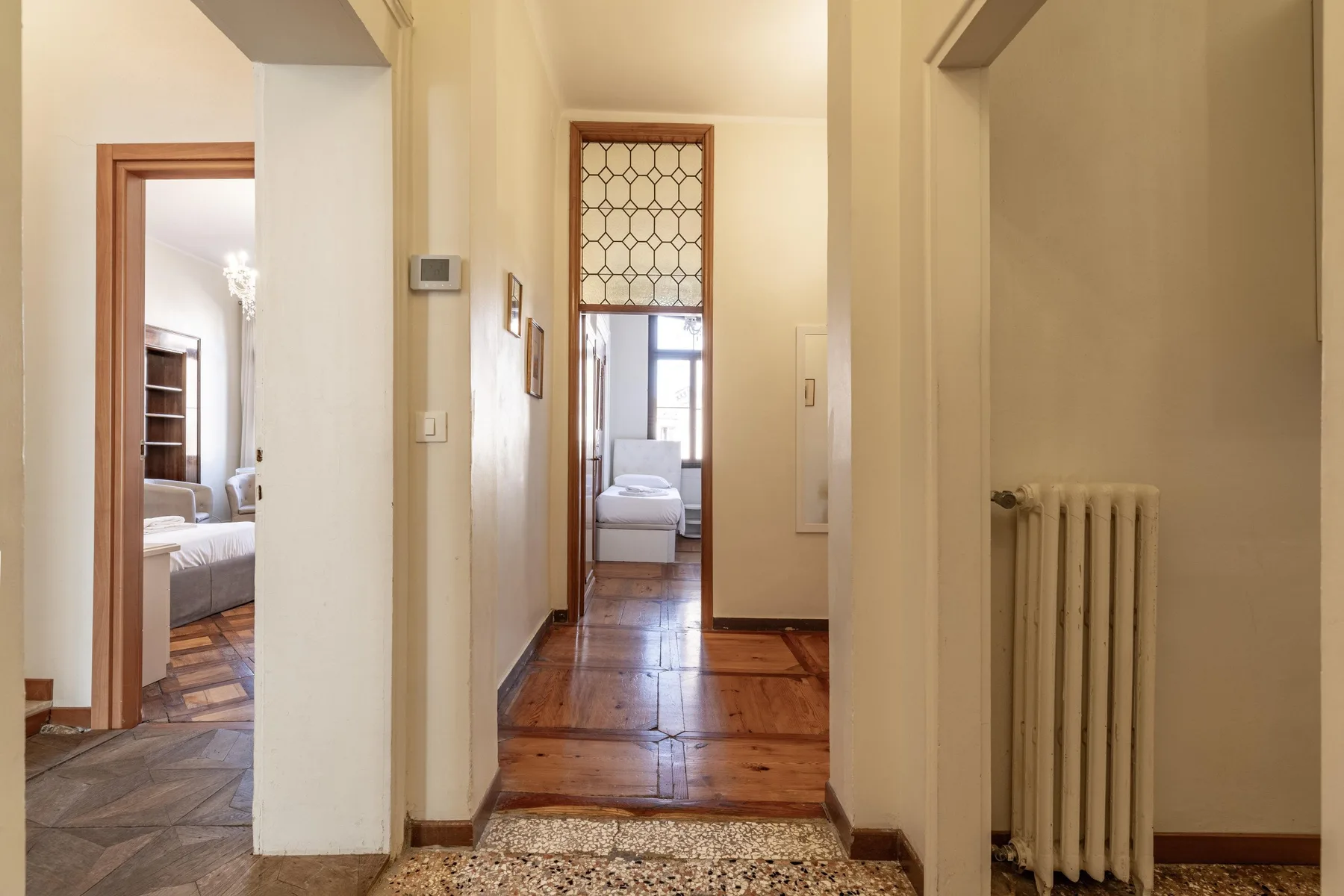 A hallway with wooden floors leads to a bright room with a window.