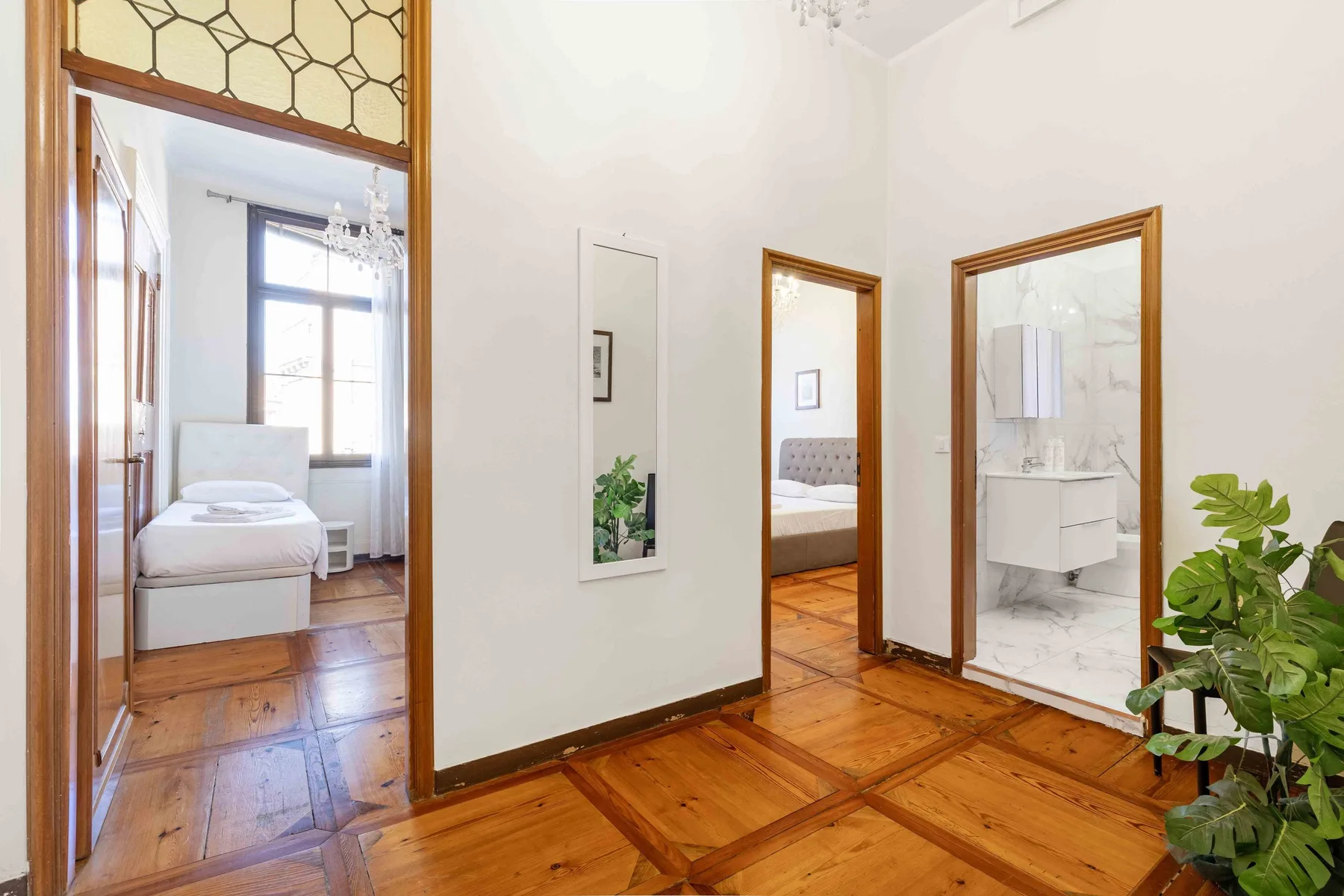A bright bedroom and adjoining bathroom open onto a polished wood hallway.