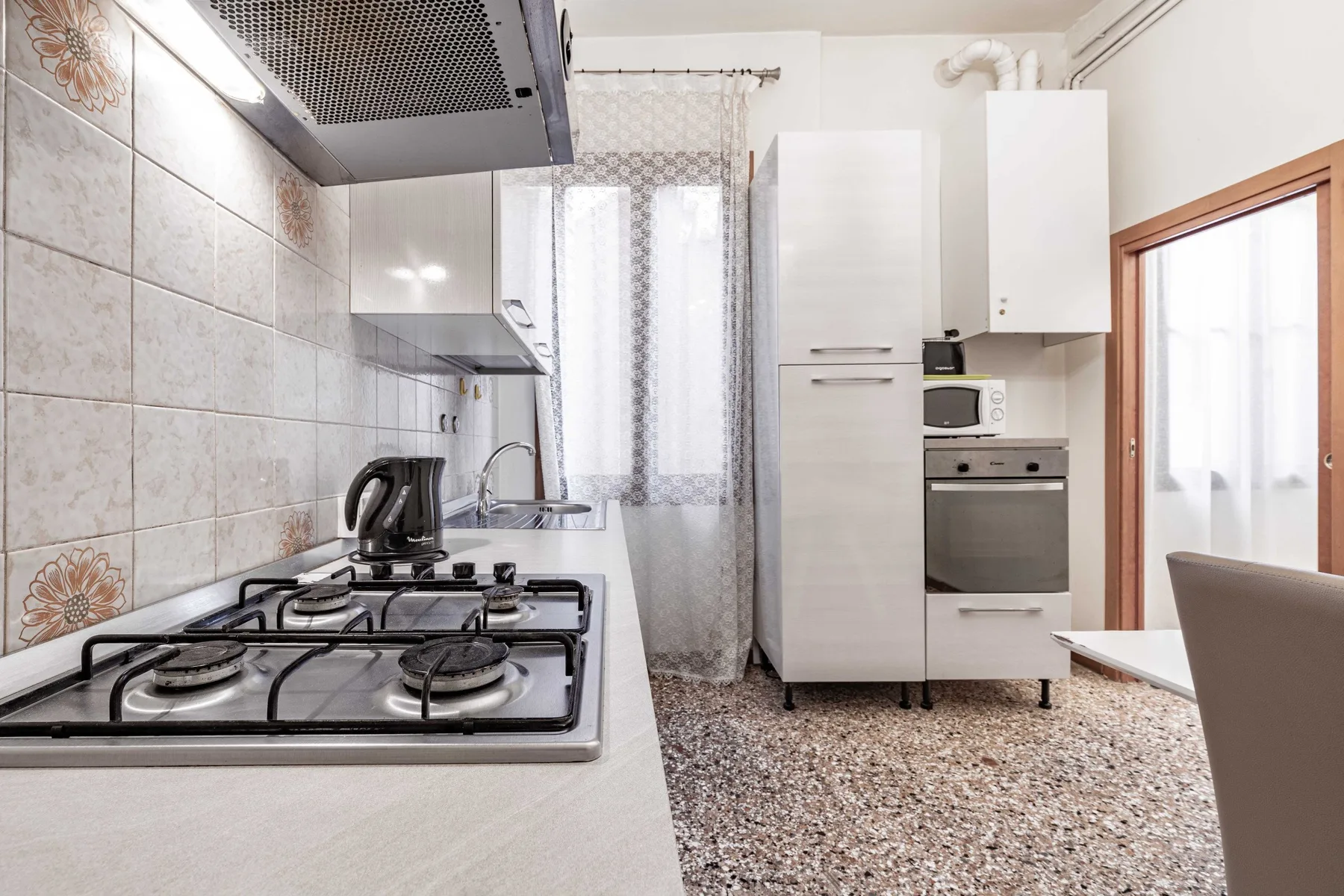 A kitchen with a gas cooktop, oven, and cabinets beside a curtained window.