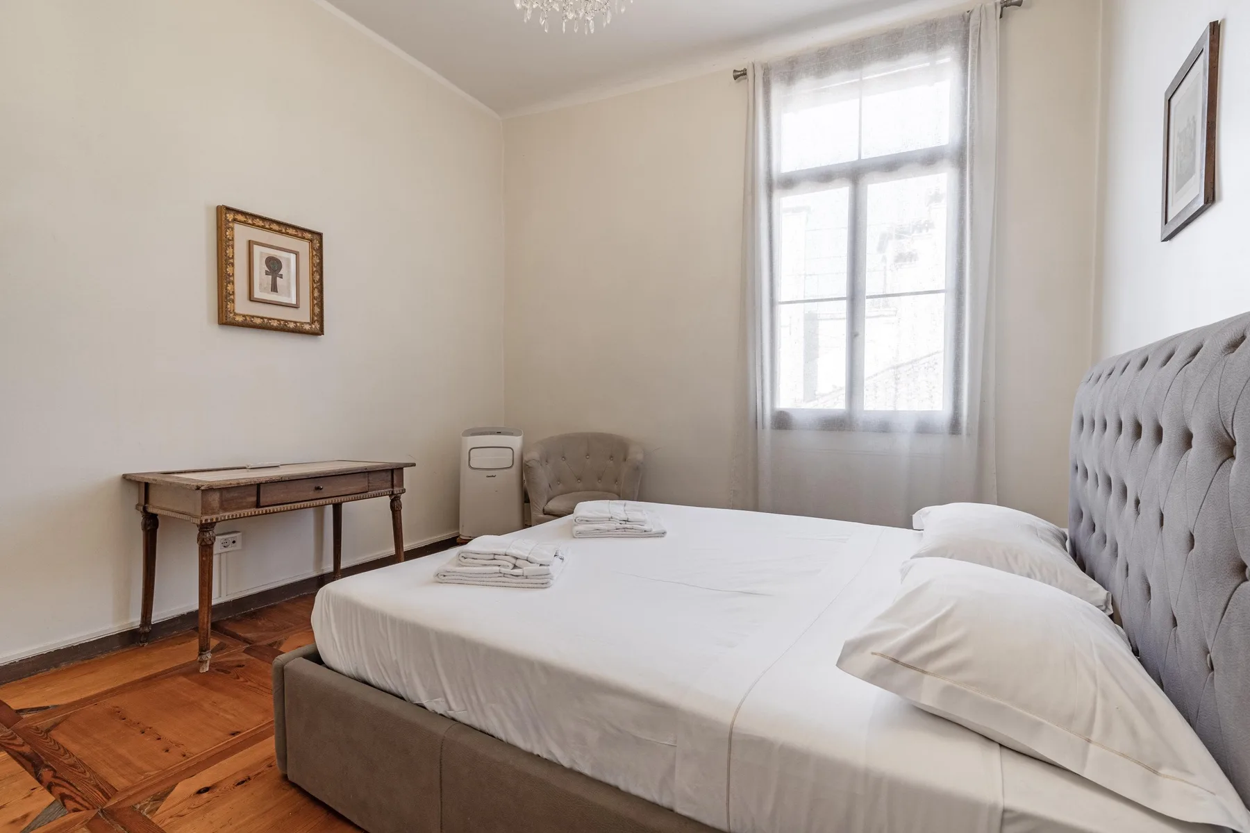 A bedroom with a large bed, a small table, and a bright window.